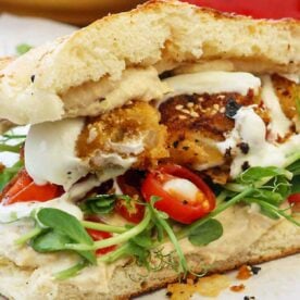 A closeup view of sweet potato falafel in a sandwich with bean shoots, cherry tomatoes and hummus.