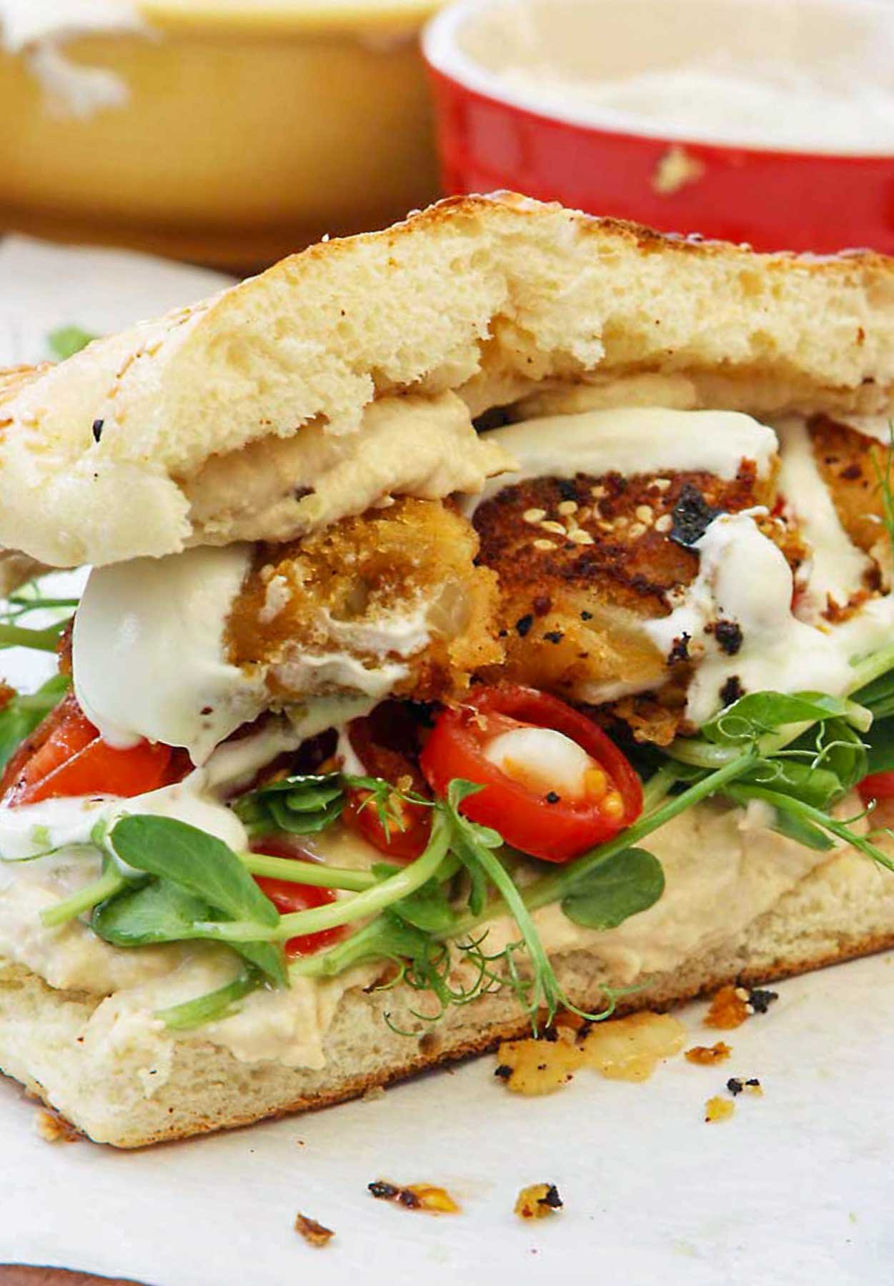 A closeup view of sweet potato falafel in a sandwich with bean shoots, cherry tomatoes and hummus.