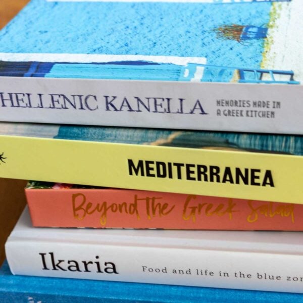 A small stack of Greek cookbooks on their sides, on a wooden table.