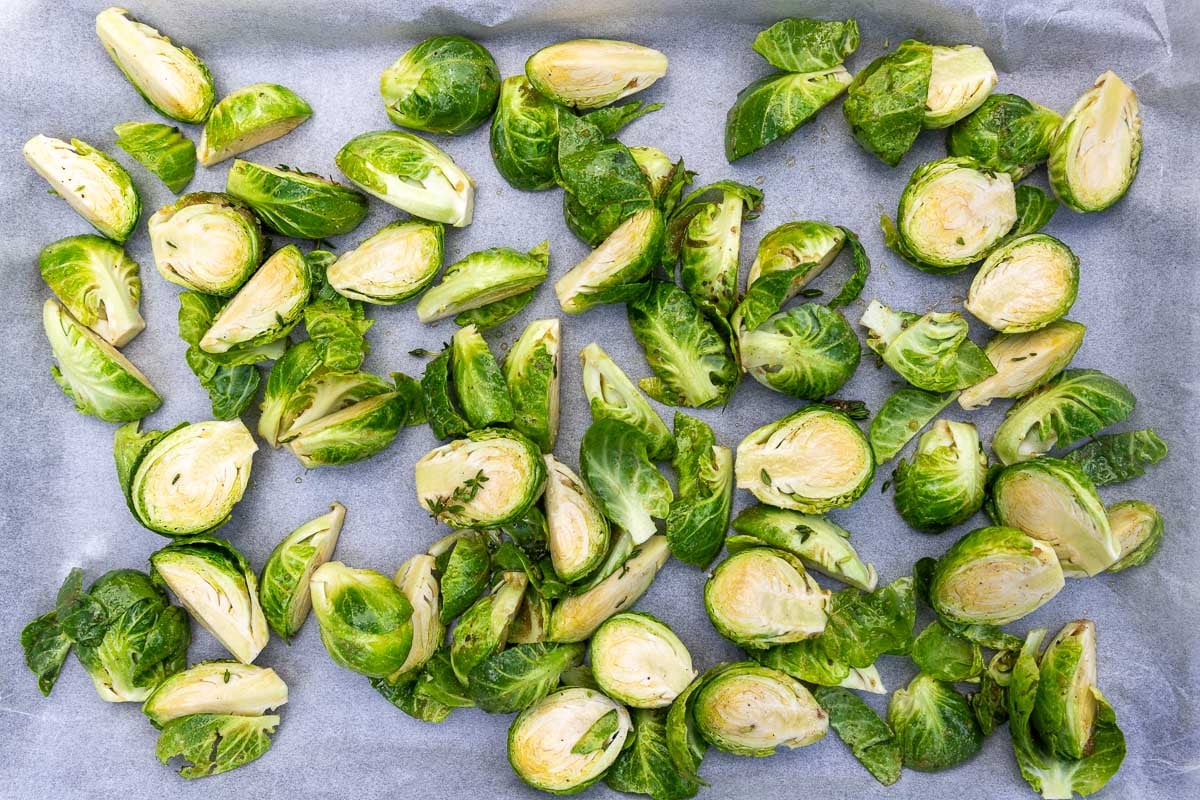 Topped, tailed brussels sprouts cut into halves or quarters and scattered across a lined baking sheet.