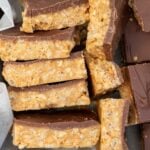 A closeup of a stack of peanut butter chocolate crunch bars on their sides in a lined baking pan.