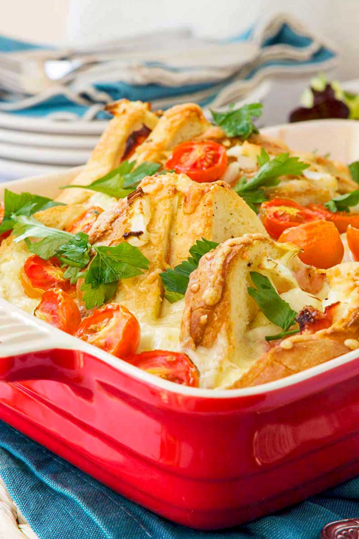 A red baking dish with a ham cheese and egg bake in it with cherry tomatoes and parsley on top.