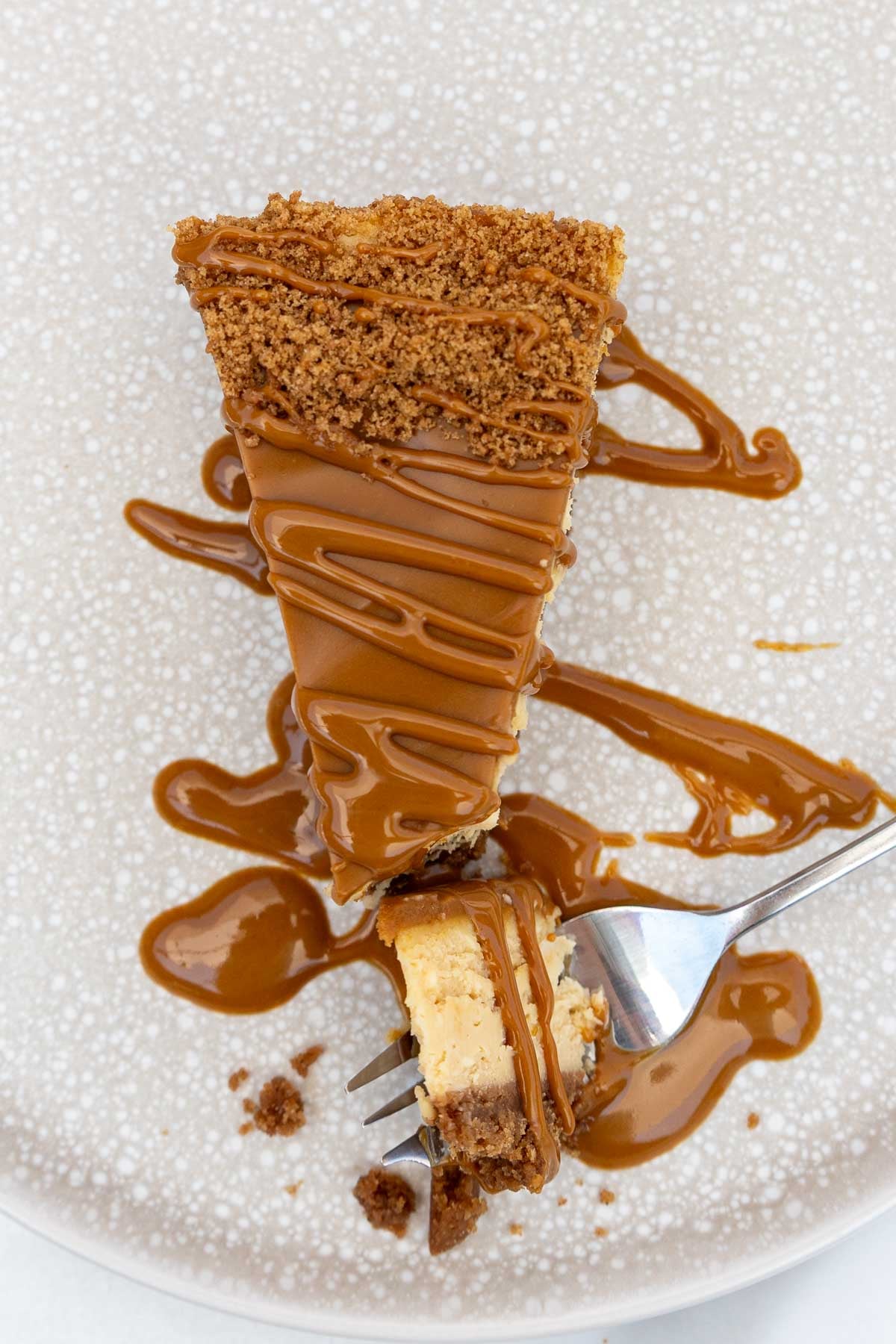 Overhead view of a single piece of the cheesecake with more melted Biscoff spread drizzled over the top, with a fork cutting off a piece.