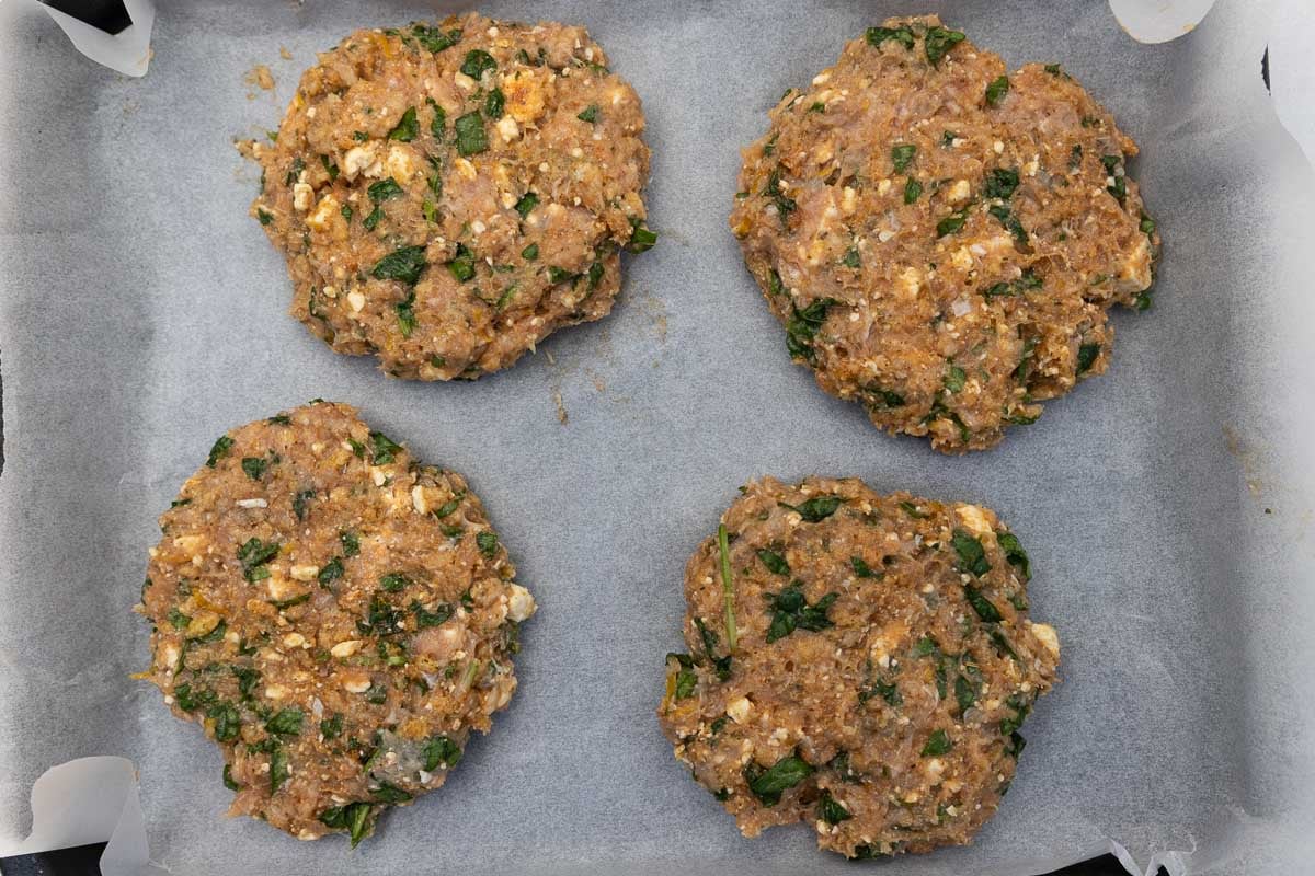 Overhead view of four unbaked spinach feta chicken burgers on baking paper.
