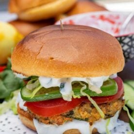A spinach and feta chicken burger with salad and tzatziki inside on a napkin with ingredients scattered around.