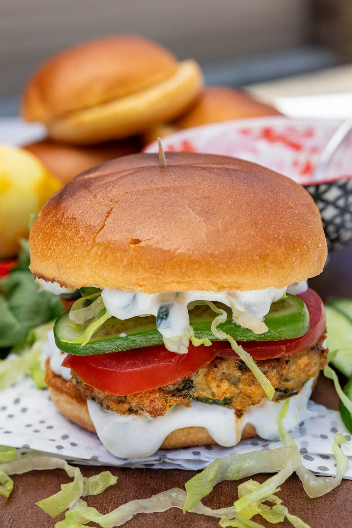 A spinach and feta chicken burger with salad and tzatziki inside on a napkin with ingredients scattered around.