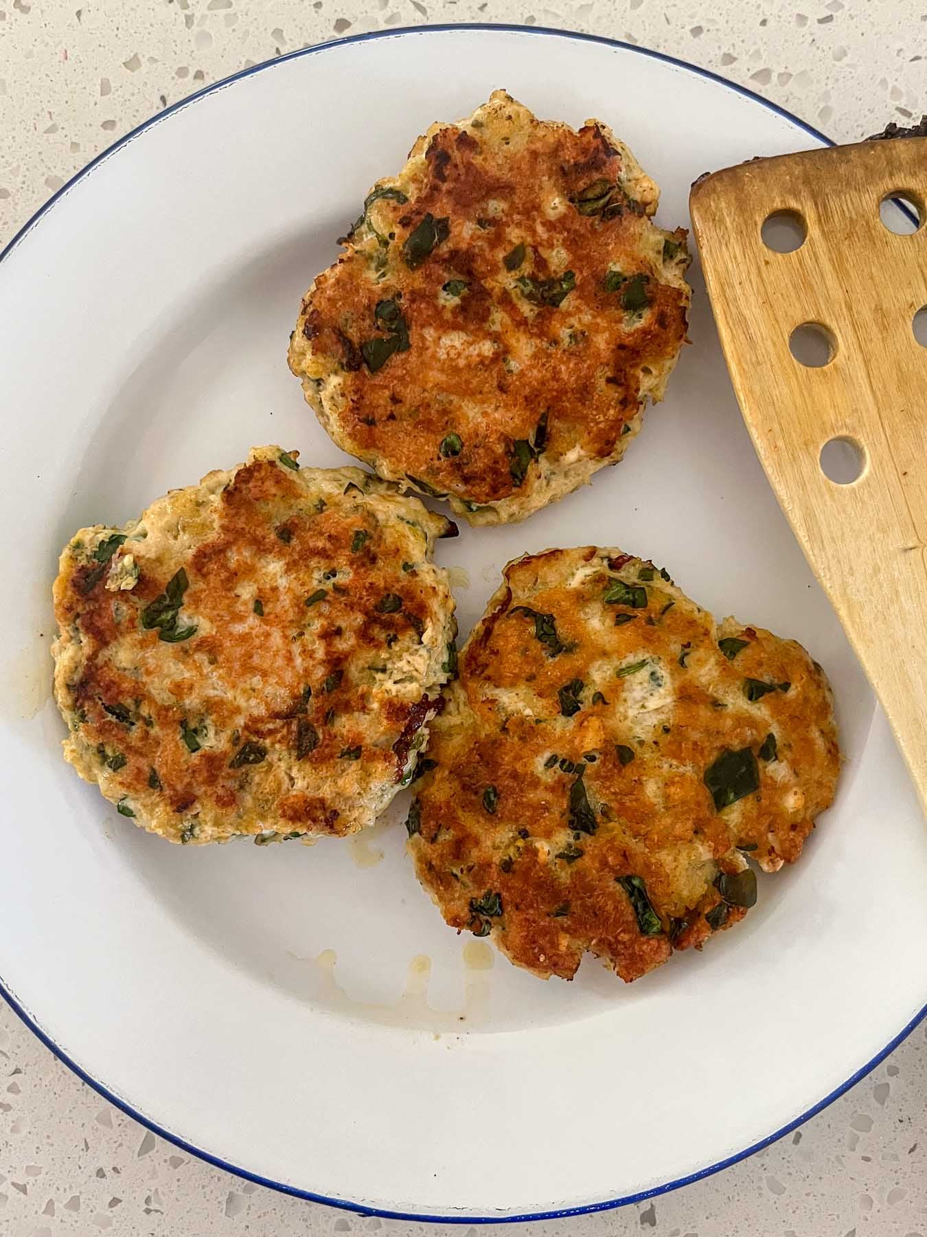 Overhead view of three of the pan-fried burgers, on a blue-rimmed white plate.