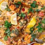Closeup of the top of the dish sprinkled with parsley and dotted with lemon segments, with a serving spoon.