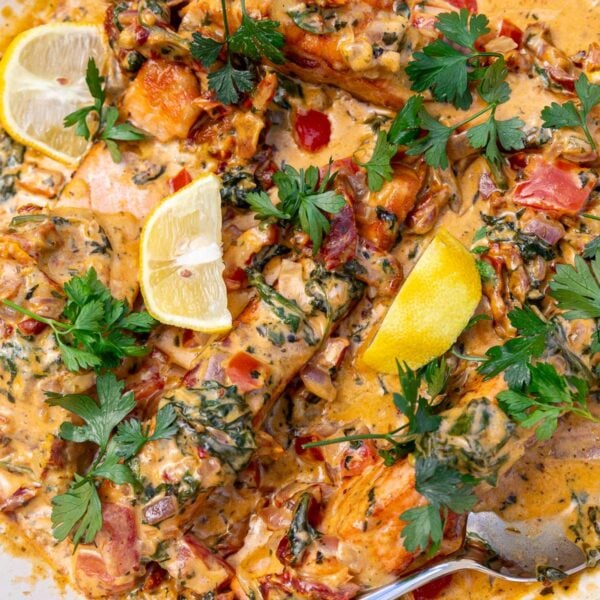 Closeup of the top of the dish sprinkled with parsley and dotted with lemon segments, with a serving spoon.