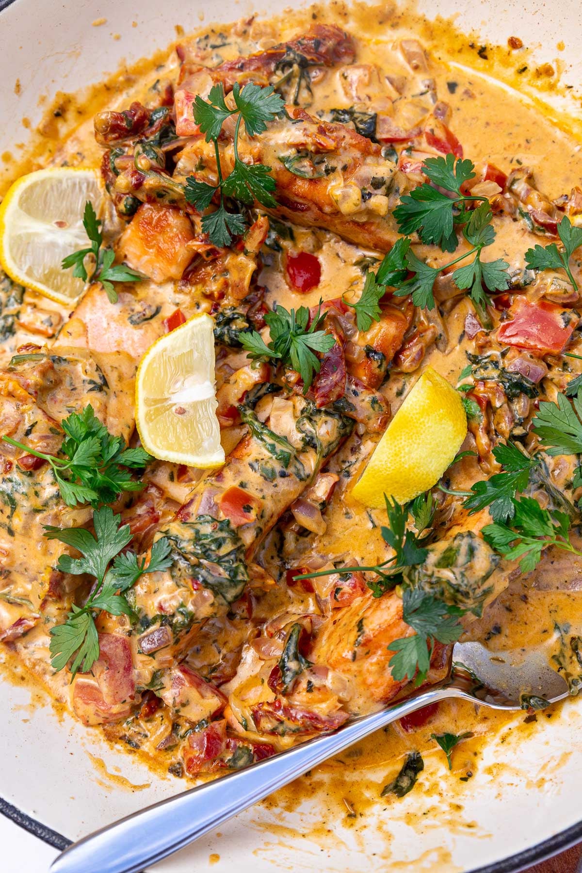 Closeup of the top of the dish sprinkled with parsley and dotted with lemon segments, with a serving spoon.