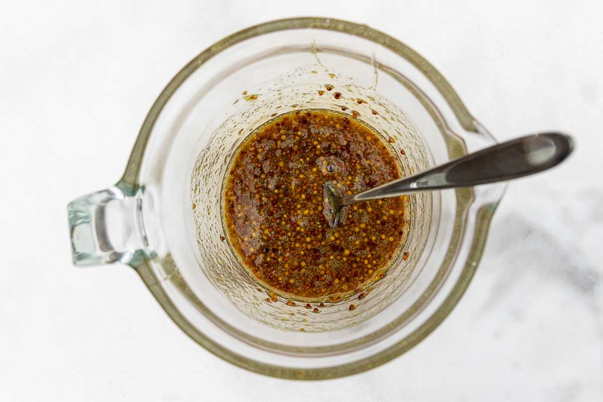 An overhead image of a glass jug of wholegrain mustard, Dijon mustard, honey and vinegar.