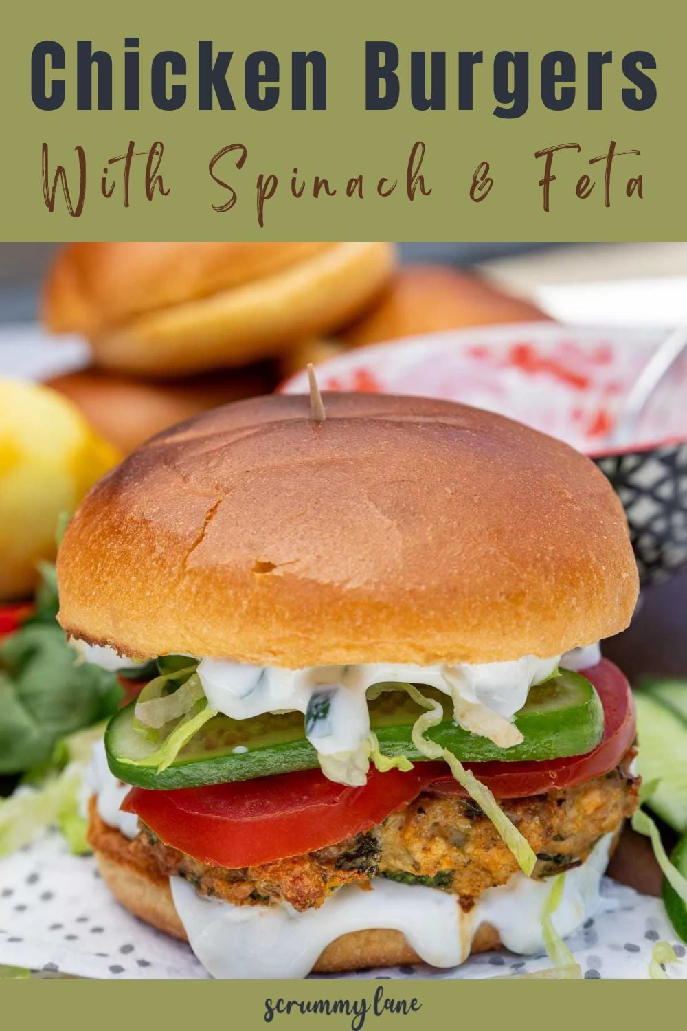 A spinach and feta chicken burger with salad and tzatziki inside with a title on a green background for Pinterest.