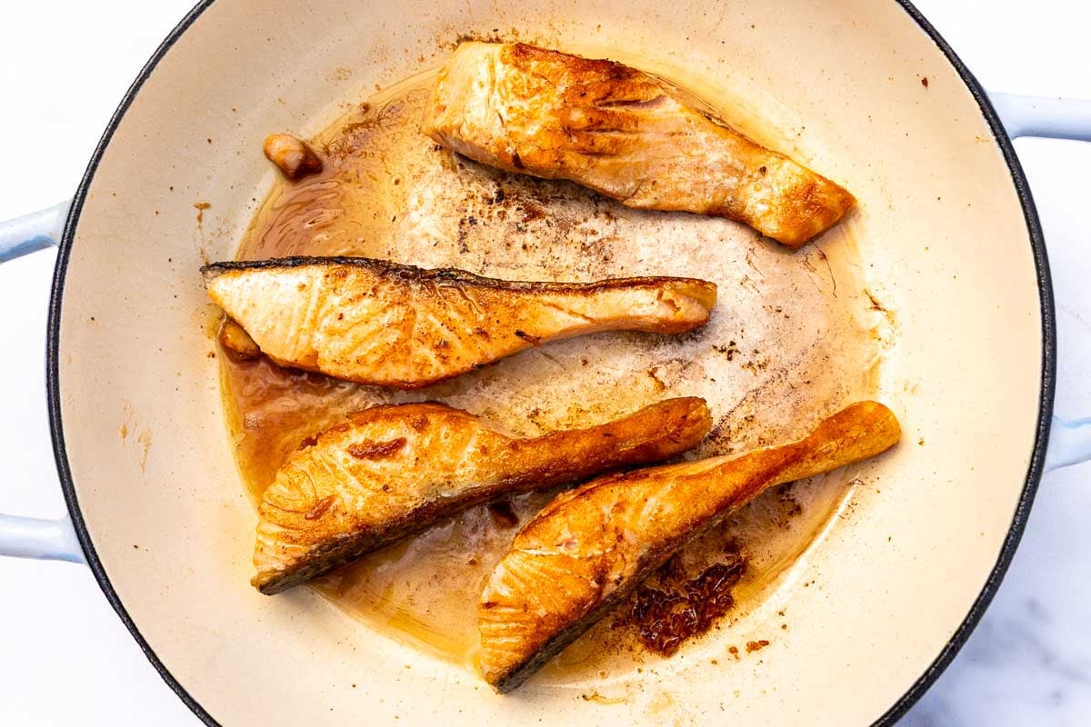Four pieces of cooked salmon in a pan.