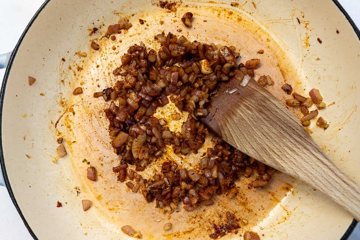 Overhead of chopped cooked onions and spices in a cast iron pan with a wooden spoon.