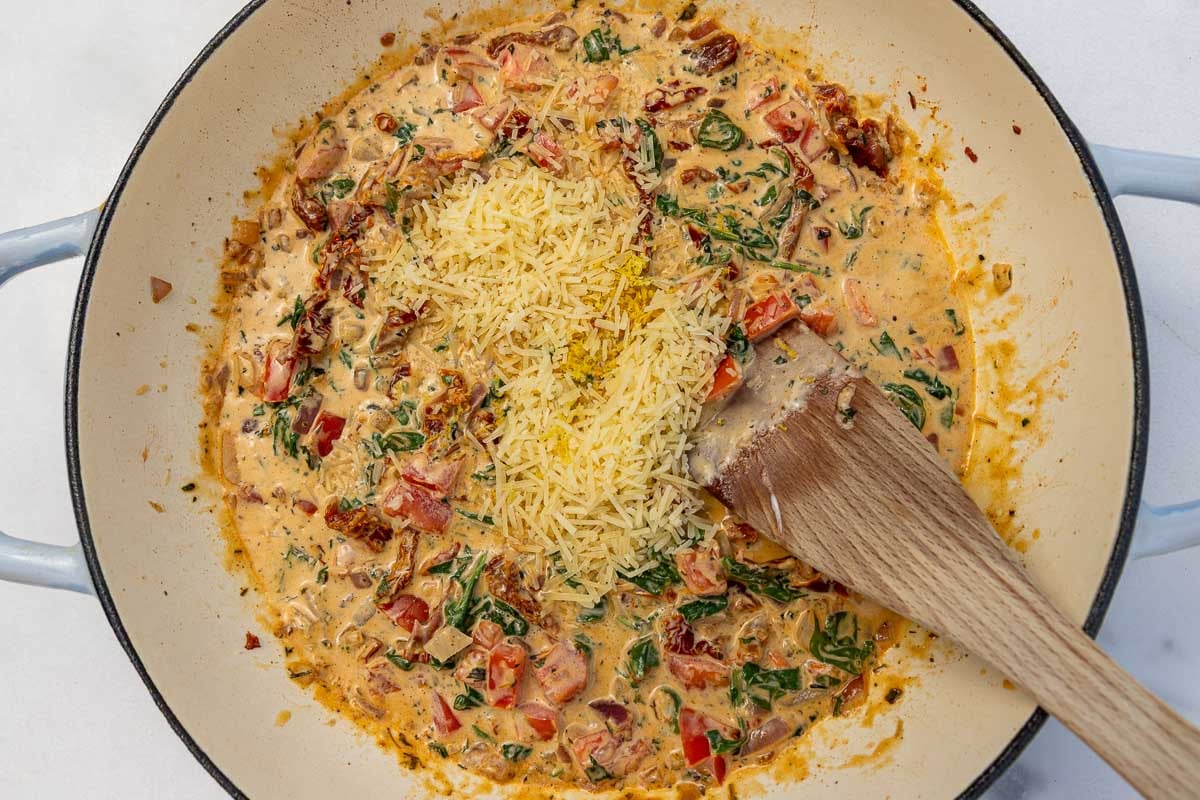 Overhead of a pan of the cream tomato sauce, with parmesan on the top and a wooden spoon.