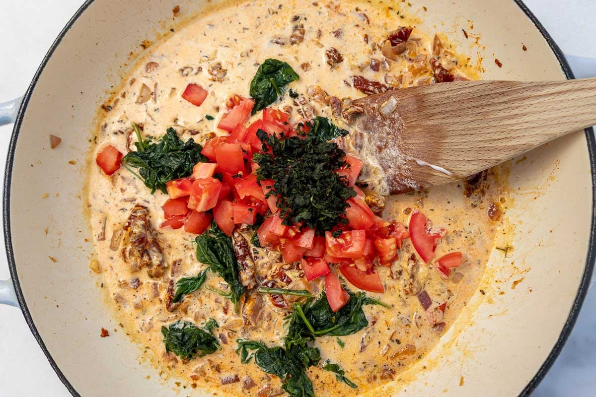 Overhead of ingredients for the sauce in a large cast iron pan with a wooden spoon.