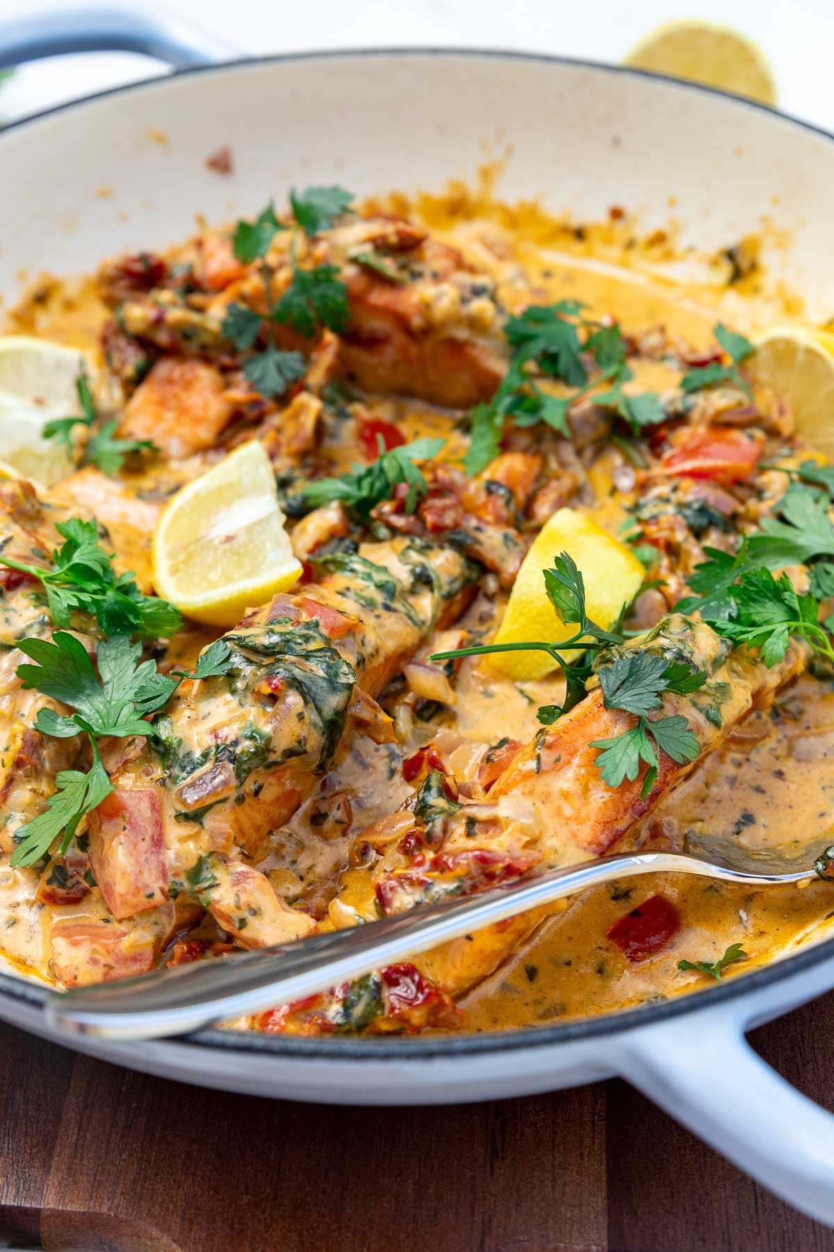 Closeup of salmon in a pan with a cream tomato sauce in a light blue pan and with a serving spoon.
