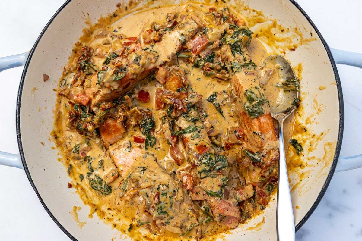 An overhead view of salmon in a tomato cream sauce in a big blue cast iron pan with a spoon.