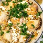 Overhead of a whole pan of chicken and orzo with fresh parsley and feta on top, and a decorative spoon in it.