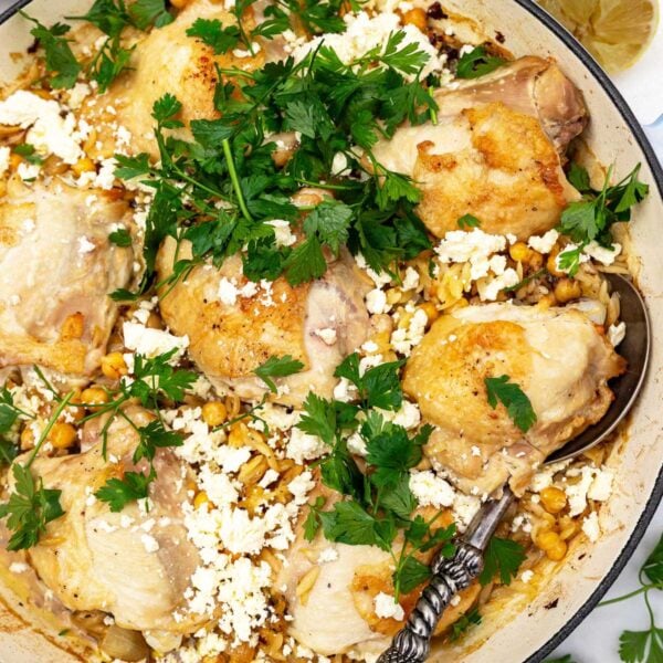 Overhead of a whole pan of chicken and orzo with fresh parsley and feta on top, and a decorative spoon in it.