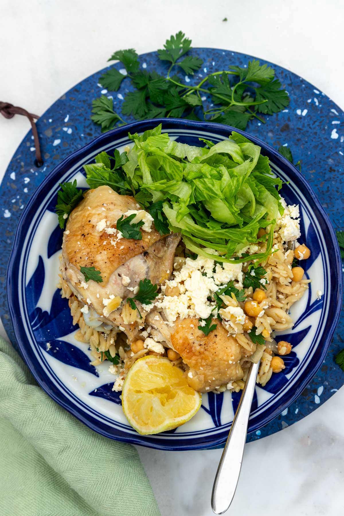 Overhead view of the food in a blue and white dish with fresh parsley and lemon on top, shredded lettuce on the side, and with a fork in it.