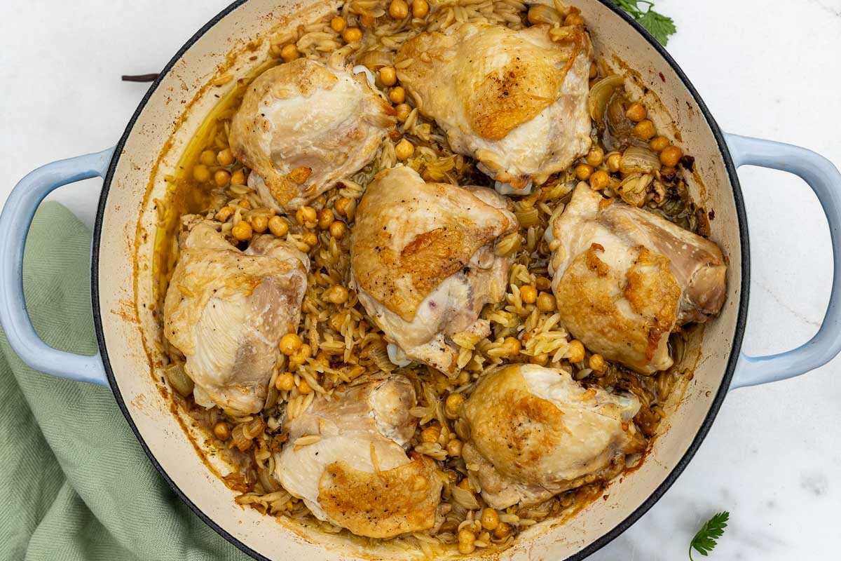 Overhead view of just-baked chicken and orzo in a light blue cast iron pan with a green tea towel.