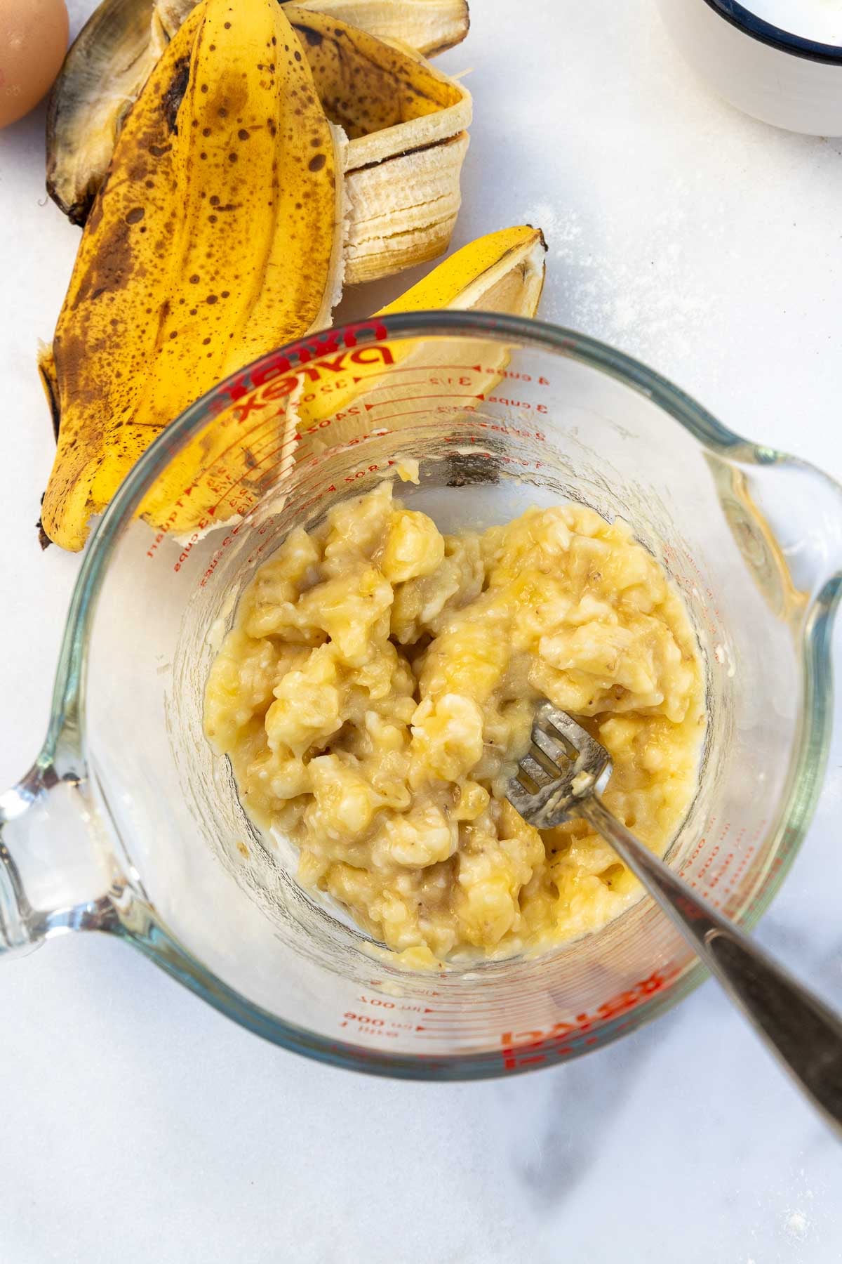 Overhead view of mashed bananas in a Pyrex jug with a fork.
