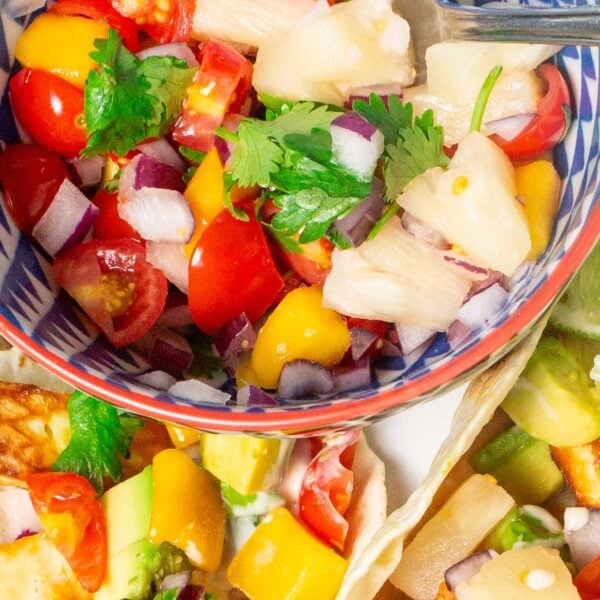 A closeup image of pineapple mango salsa in a bowl with tacos next to it with the salsa garnishing them.