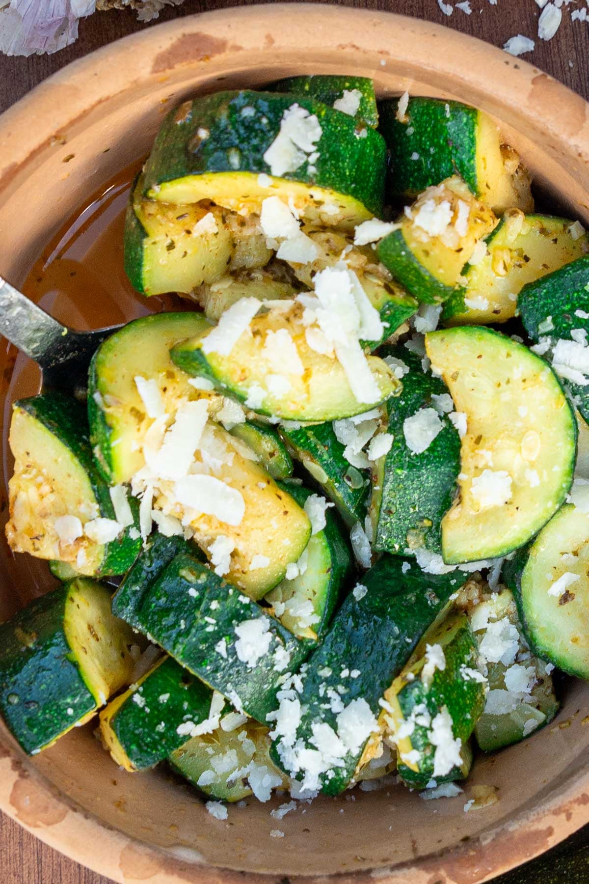 A closeup of the top of a small dish of sauteed zucchini, with parmesan cheese on top and a spoon in the dish.