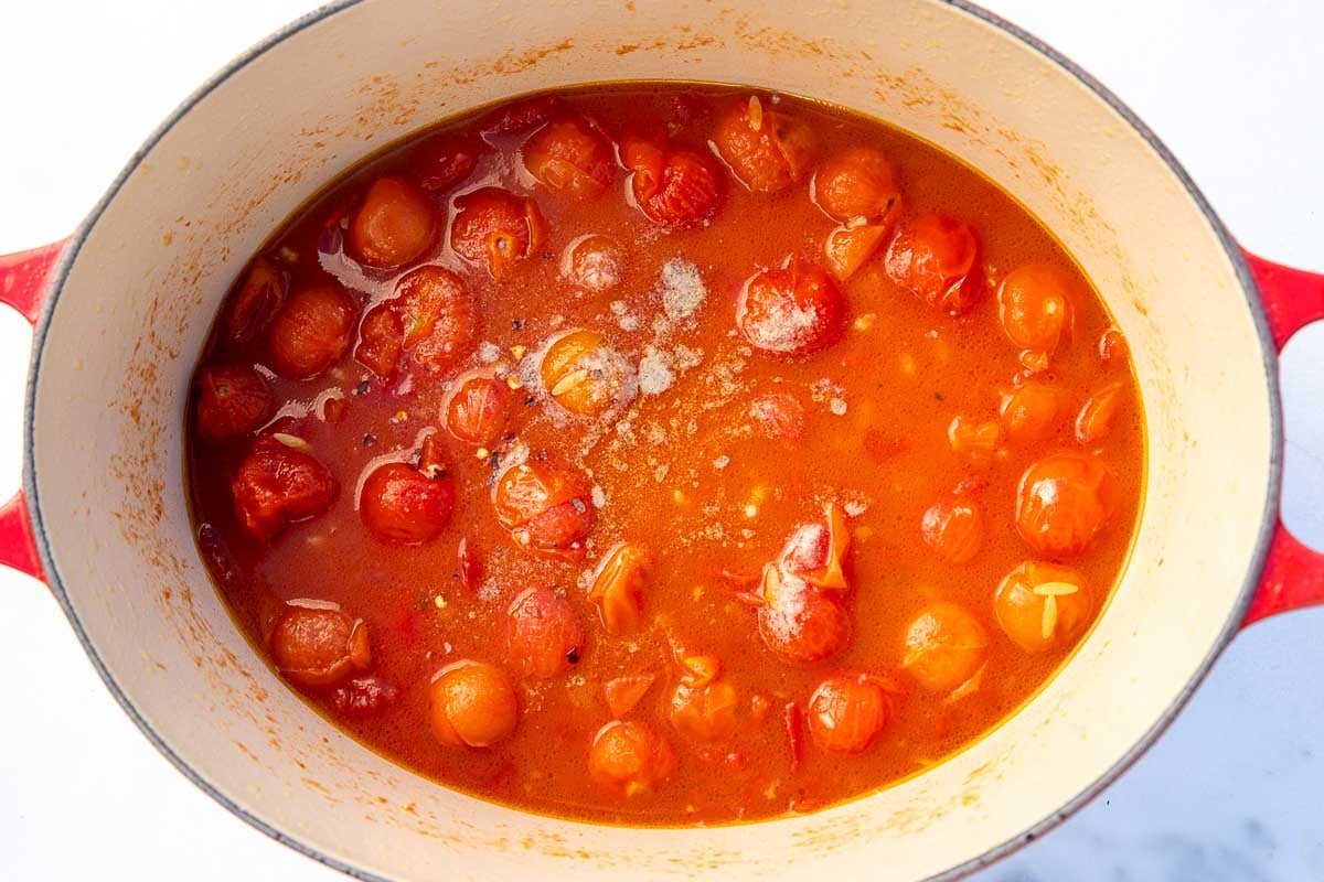 The top of the ingredients for tomato orzo in a red cast iron pot, with the tomatoes and salt and pepper visible on top.