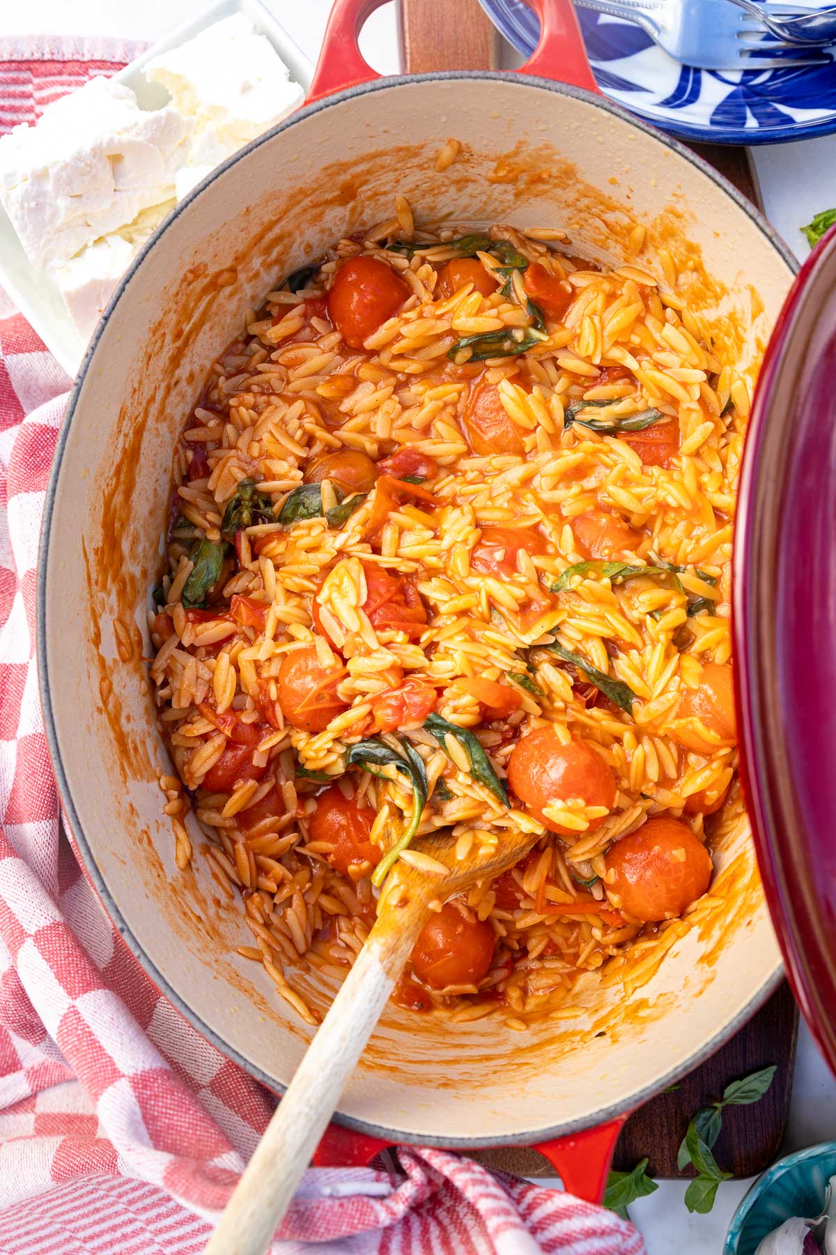 Closeup of orzo and tomatoes in a pot with a wooden spoon.