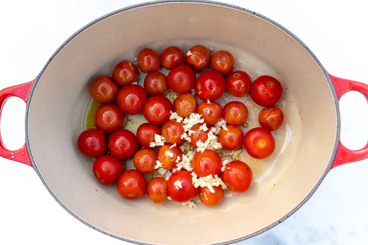 Cherry tomatoes and raw garlic in olive oil in a cast iron pot.