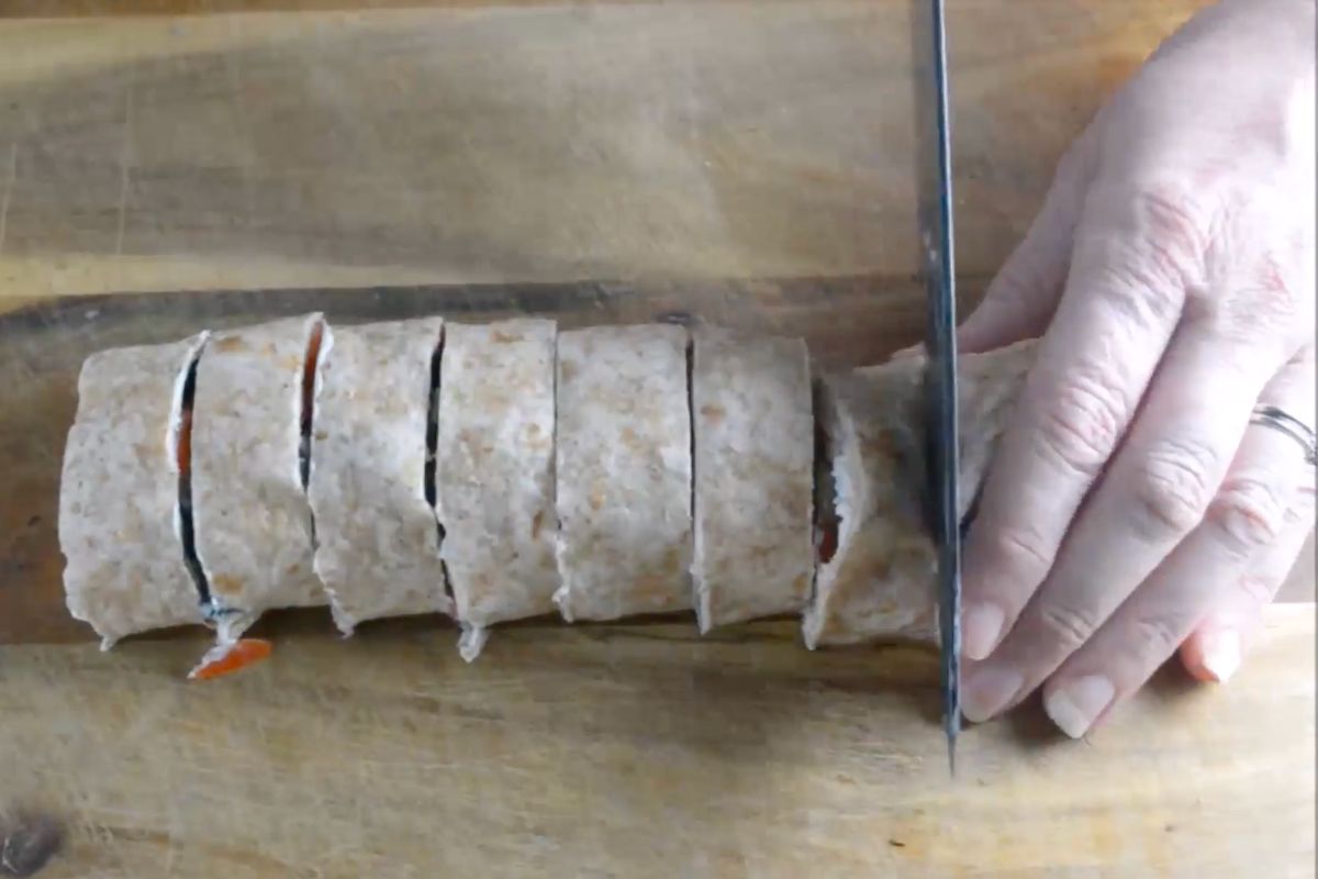 Someone cutting a rolled up tortilla with fillings with a sharp knife.