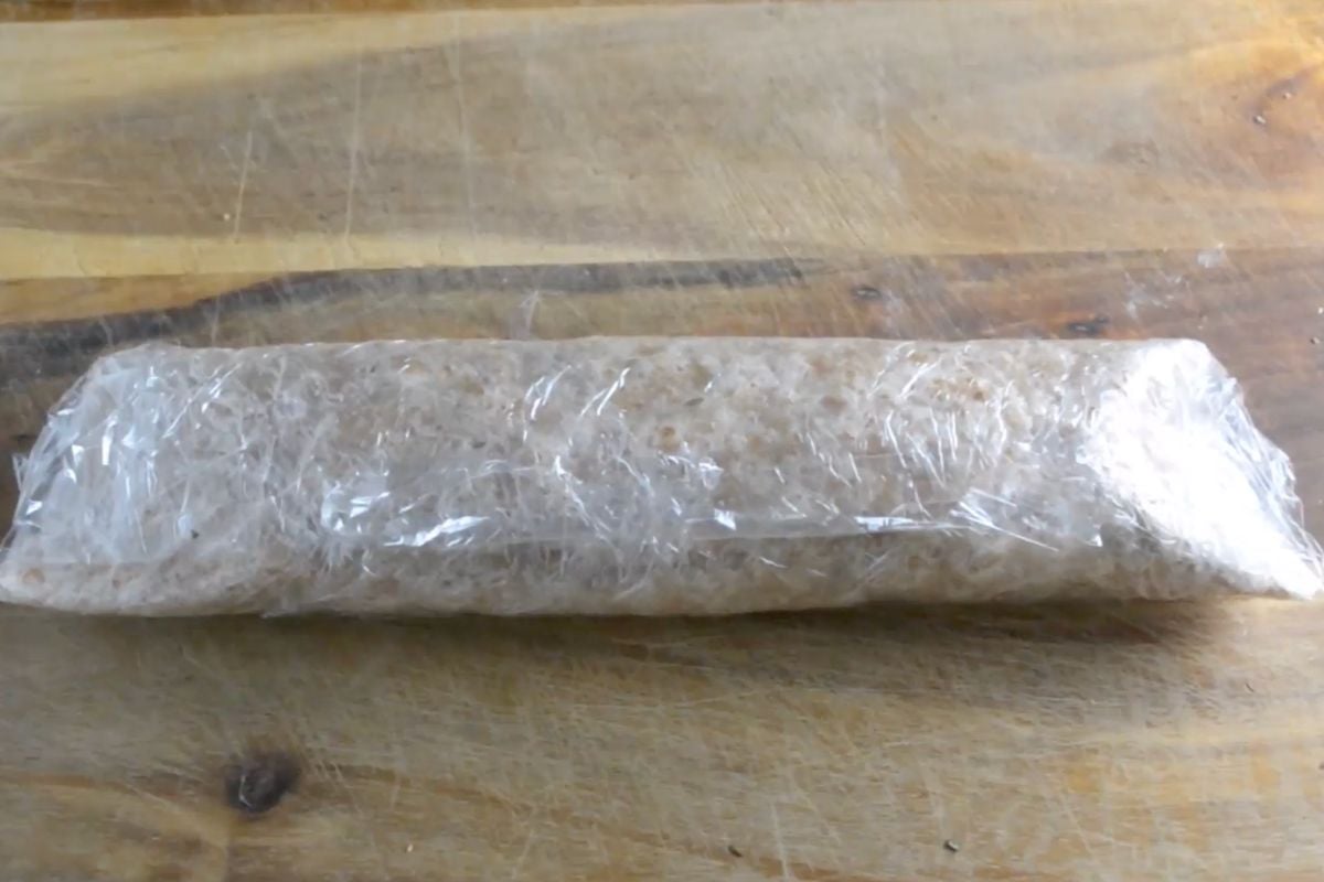 A tortilla with fillings rolled up in plastic wrap.