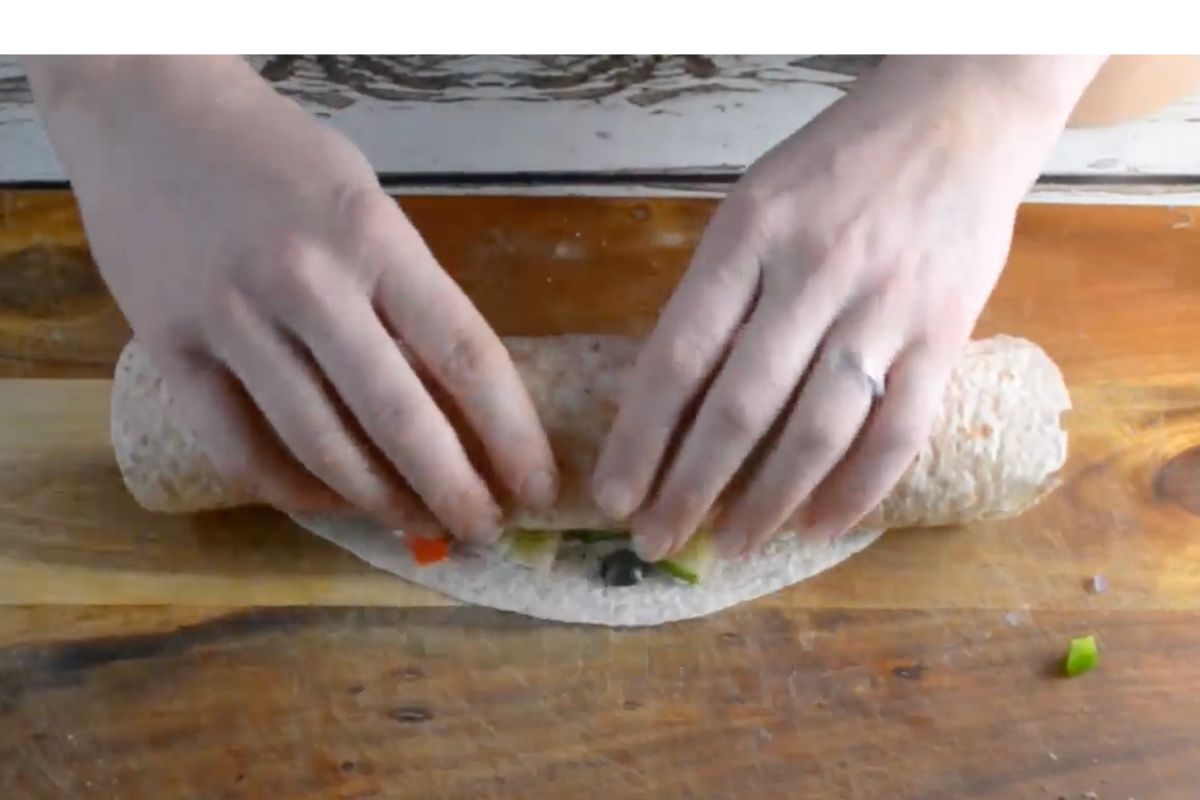 Someone rolling up a tortilla pinwheel on a wooden board.
