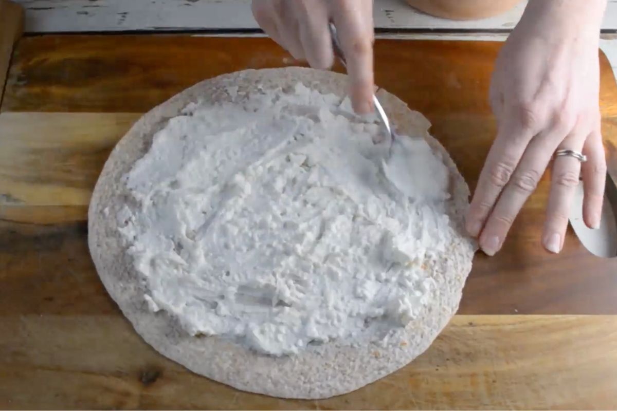 Someone spreading a cream cheese and yogurt mixture on a tortilla.