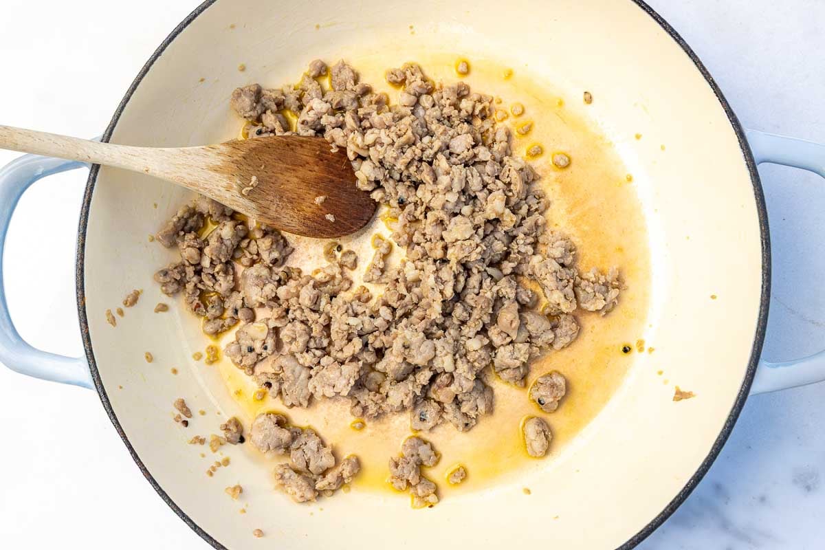 Ground Italian sausage cooked in a large pan with a wooden spoon.