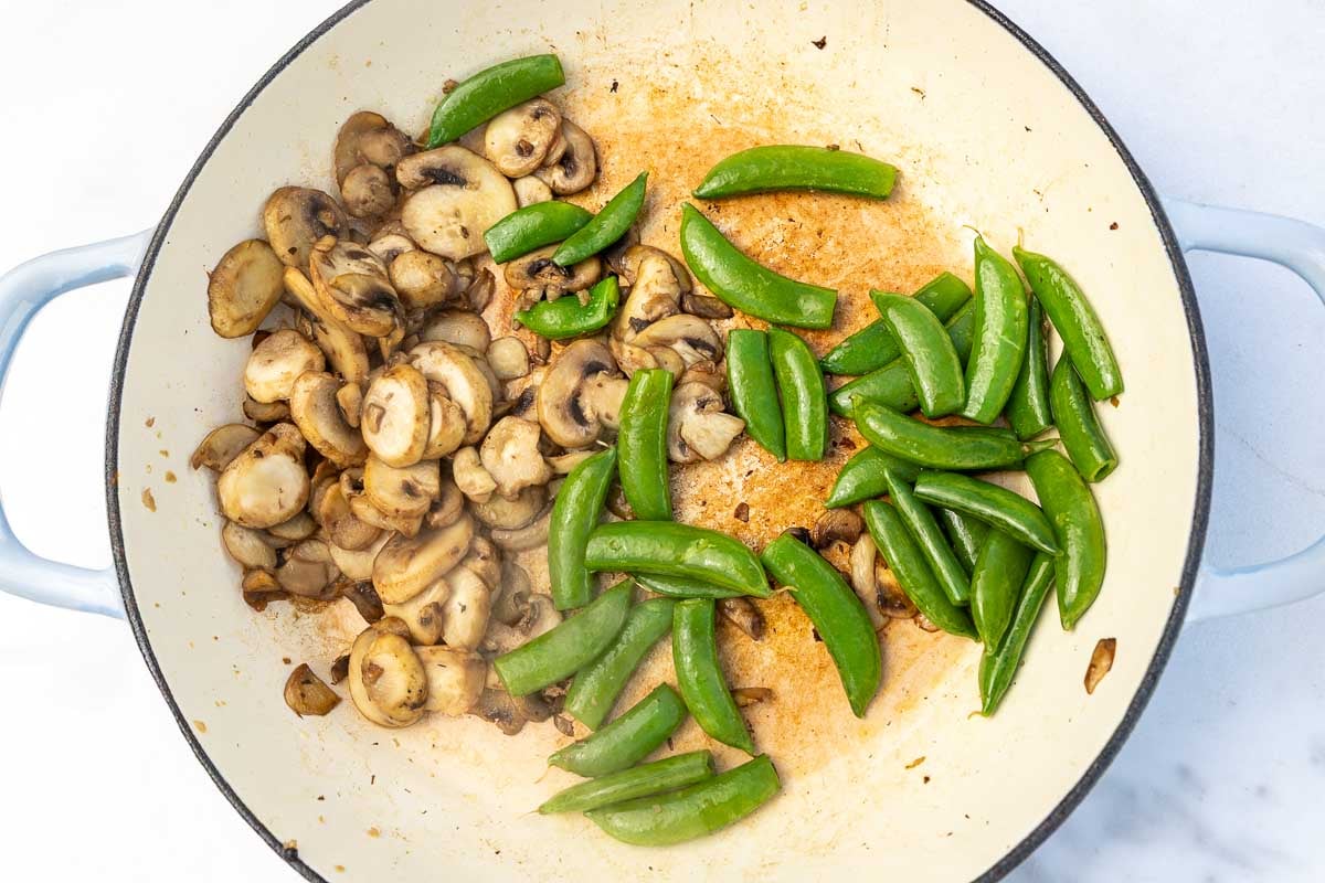 Overhead view of mushrooms and snow peas in a large pan.