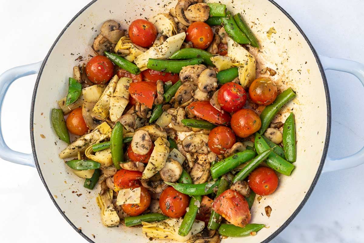 Colorful stir-fried vegetables such as tomatoes and mushrooms and snow peas in a large pan.