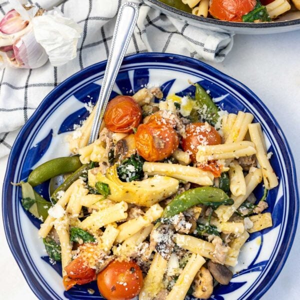 Overhead view of a blue and white dish of Italian sausage pasta with lots of colorful vegetables.