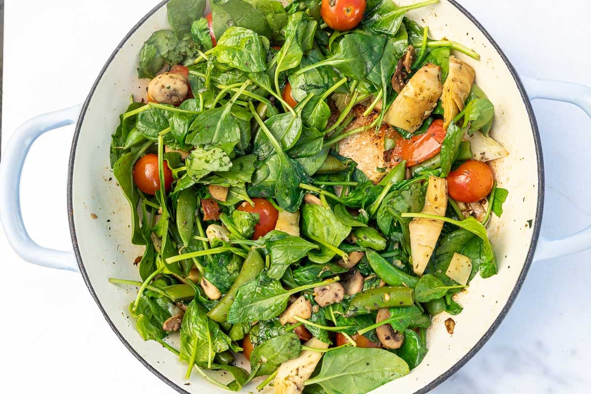 Colorful vegetables and sausage with spinach visible on top in a large pan.