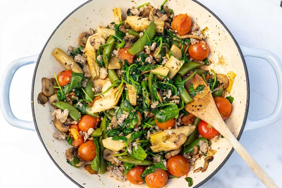A ground sausage and vegetable mixture in a big pan with a wooden spoon.