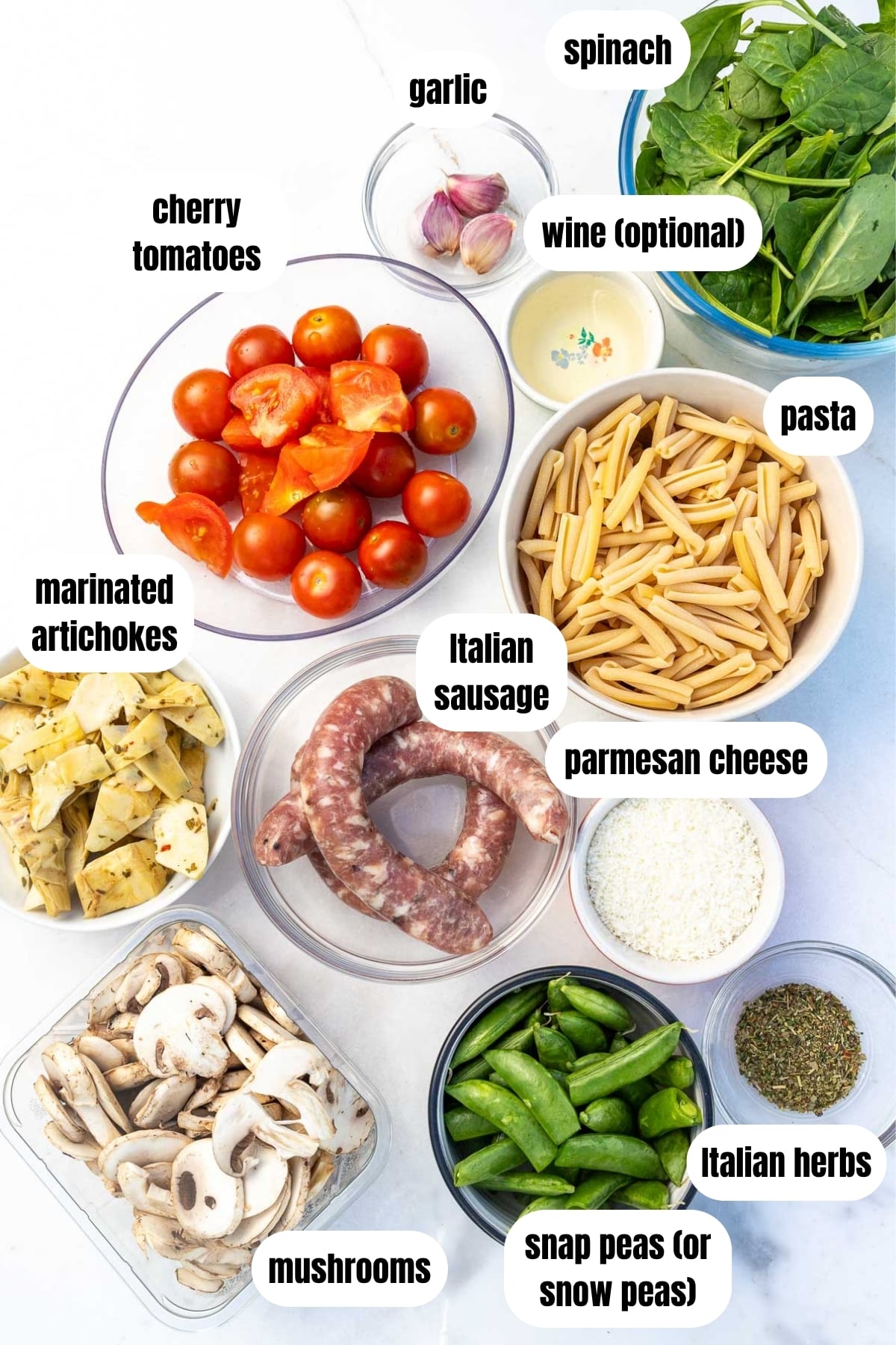Overhead view of all ingredients needed for an Italian sausage pasta dinner including Italian sausage, pasta, cherry tomatoes, mushrooms, snap peas, herbs, parmesan, artichokes, wine, spinach and garlic.