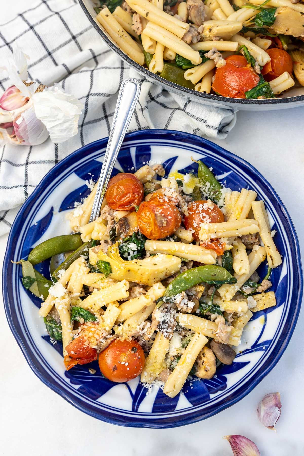 Overhead view of a blue and white dish of Italian sausage pasta with lots of colorful vegetables.